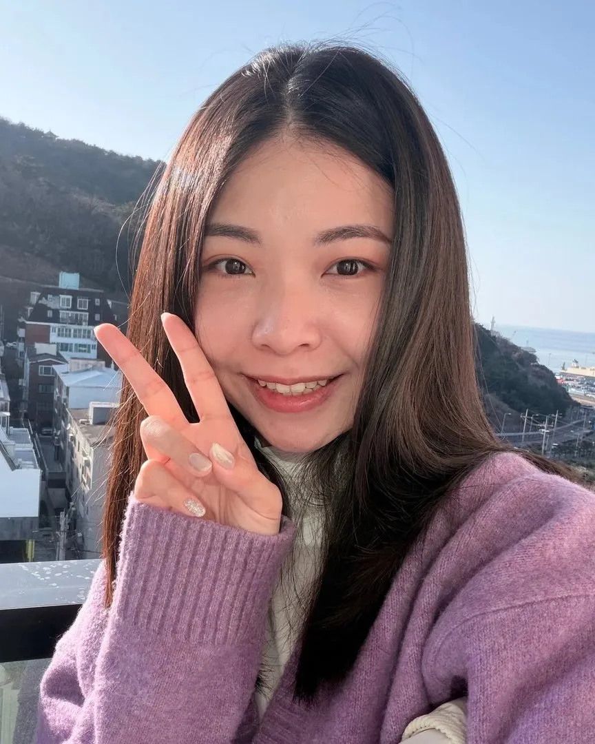釤釤穿著紫色毛衣,比著 YA 微笑